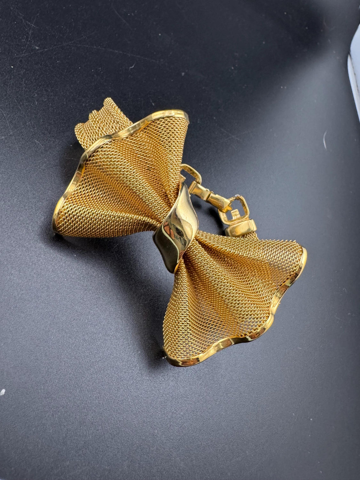 A gold-colored metal bow tie is shown against a dark background.