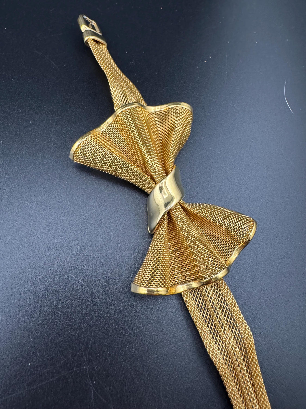 A gold mesh bow tie with a metallic band is displayed against a dark background.