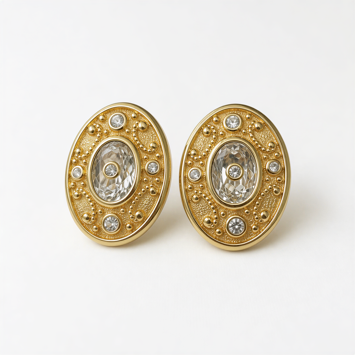 A pair of gold earrings with a central oval-shaped design and small diamonds or gemstones around the edges.