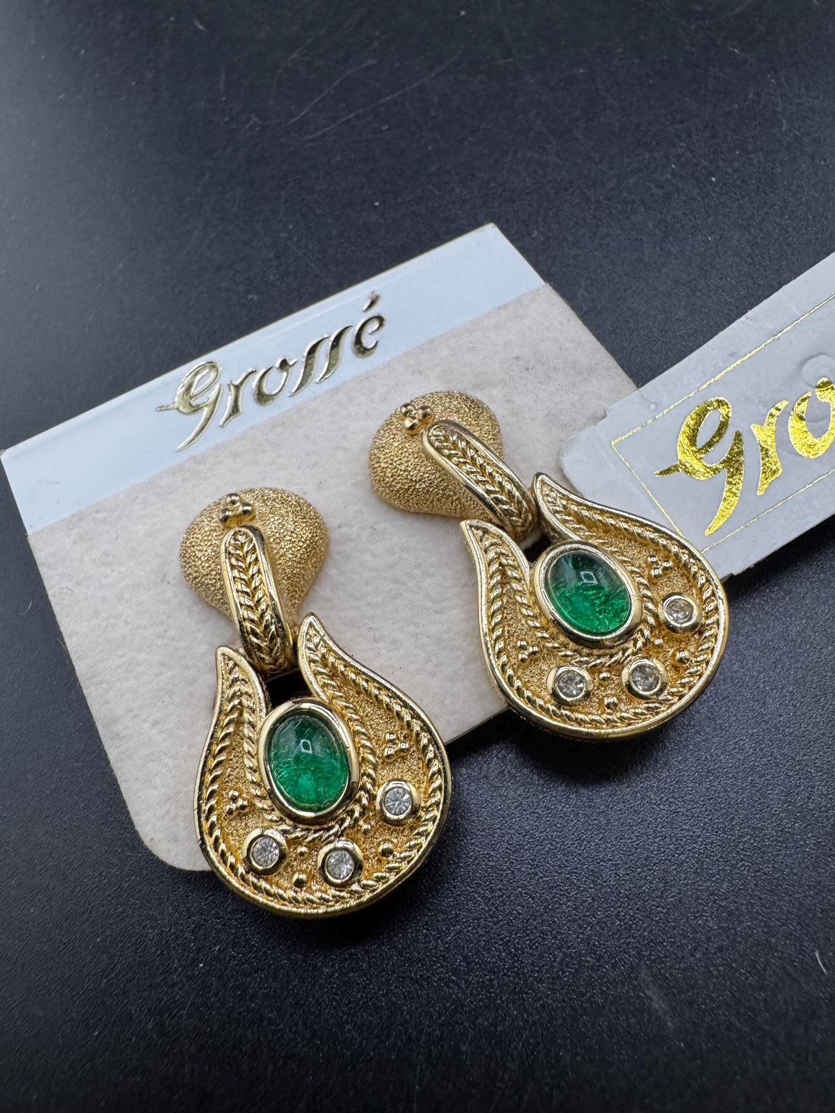 A pair of gold earrings with green gemstones, displayed on a dark background.