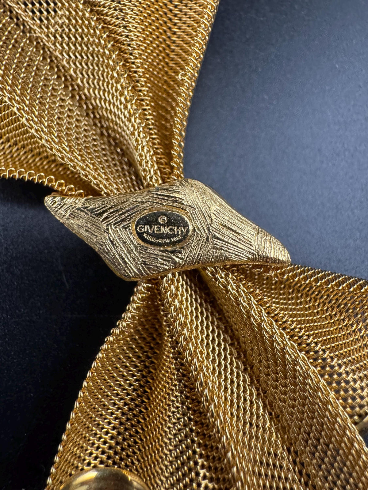 a close-up view of a gold-colored metal object, possibly a piece of jewelry or a decorative item, with a textured surface.
