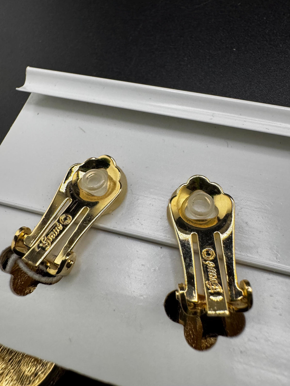 a pair of gold-colored earrings with a clear plastic piece in the center, resting on a white surface.