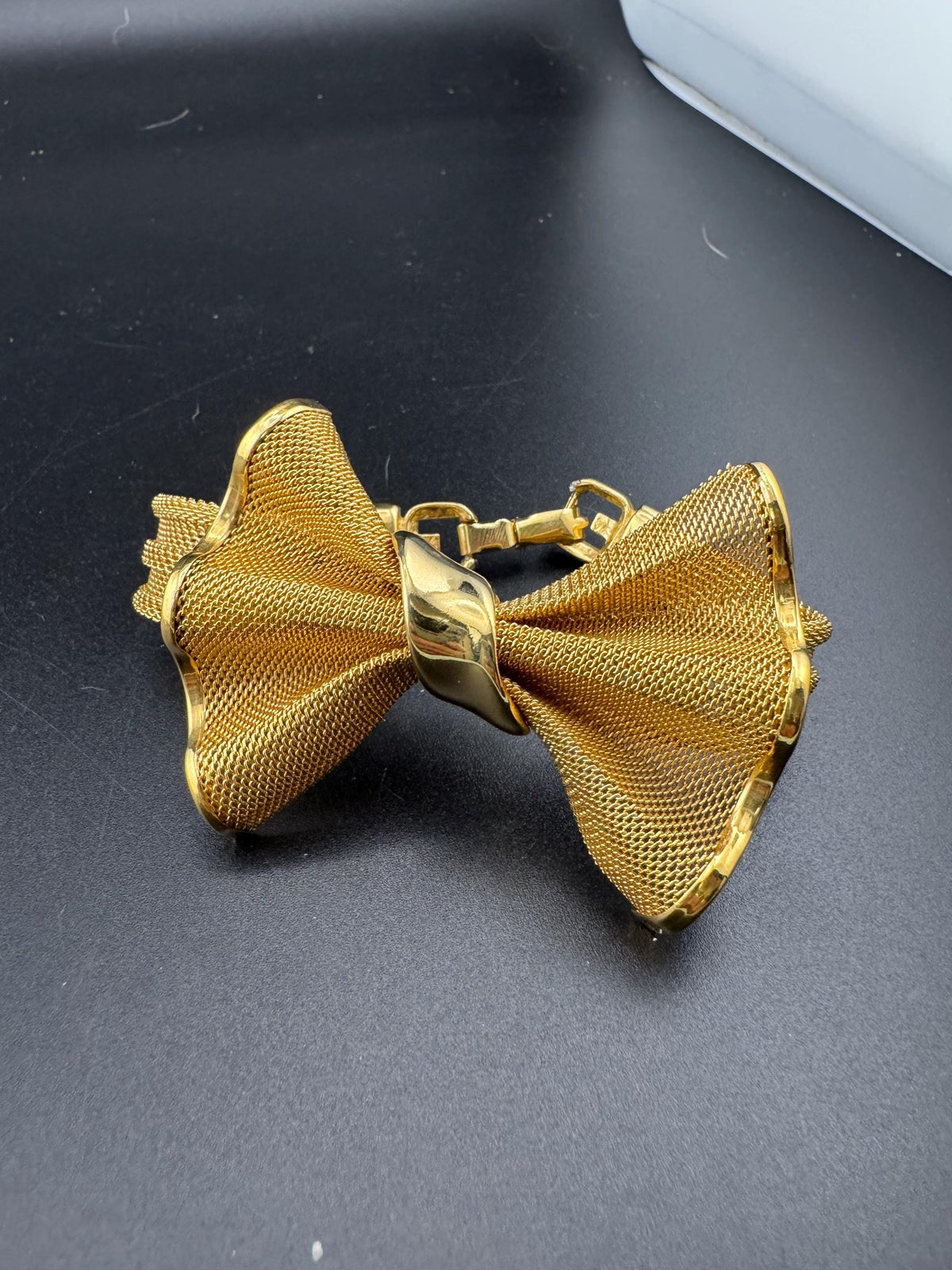 A gold-colored bow tie is displayed on a black surface.