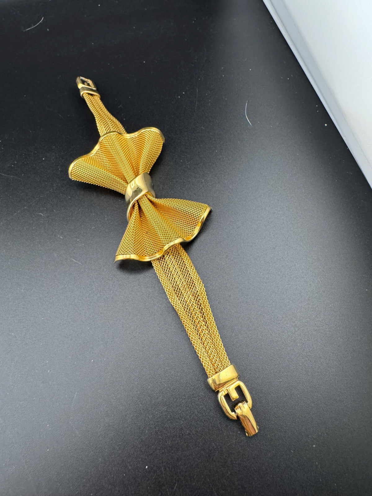 A gold-colored bow tie-like accessory is lying on a black surface.