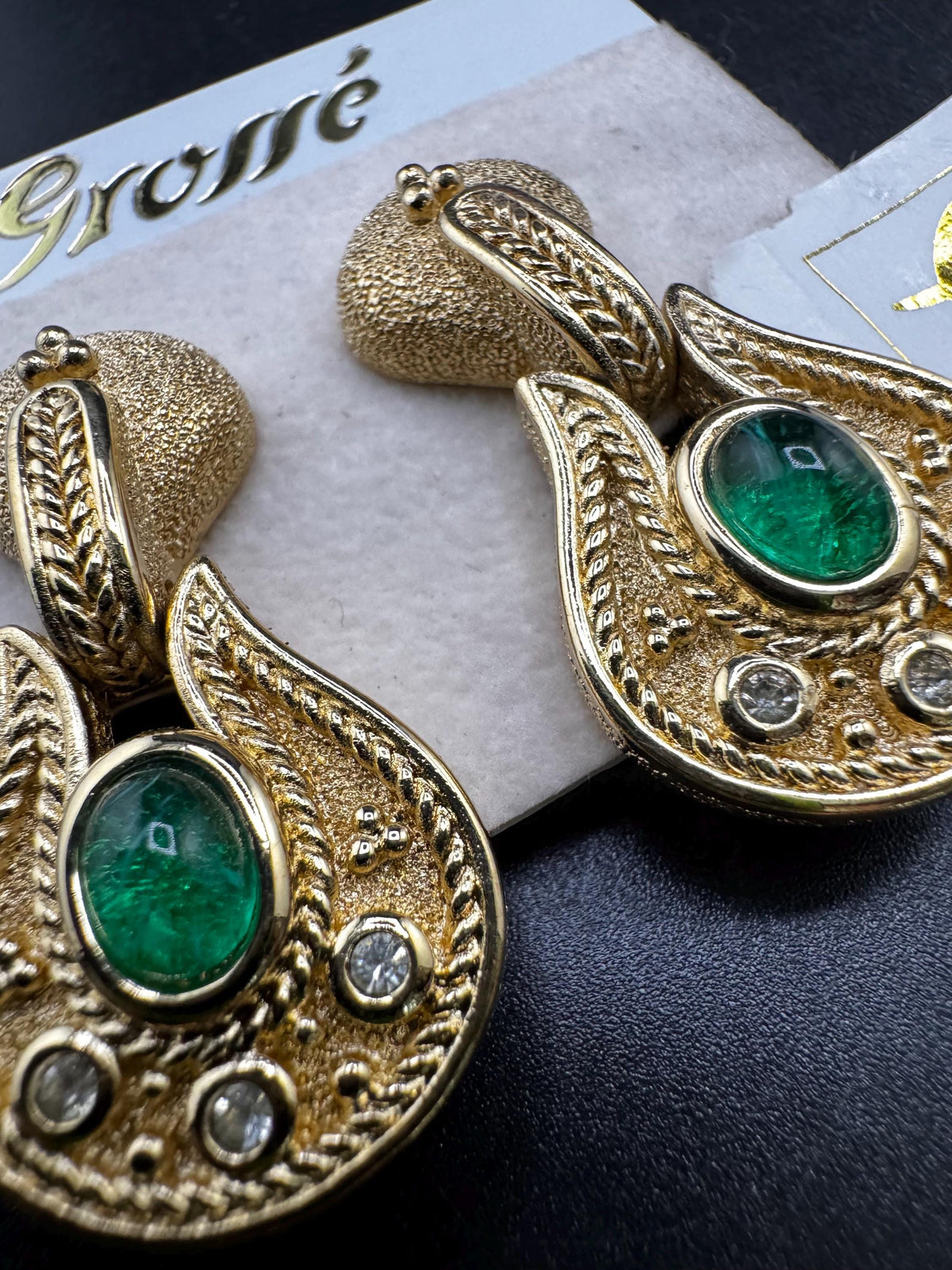 A pair of ornate gold earrings with green gemstones and intricate designs.