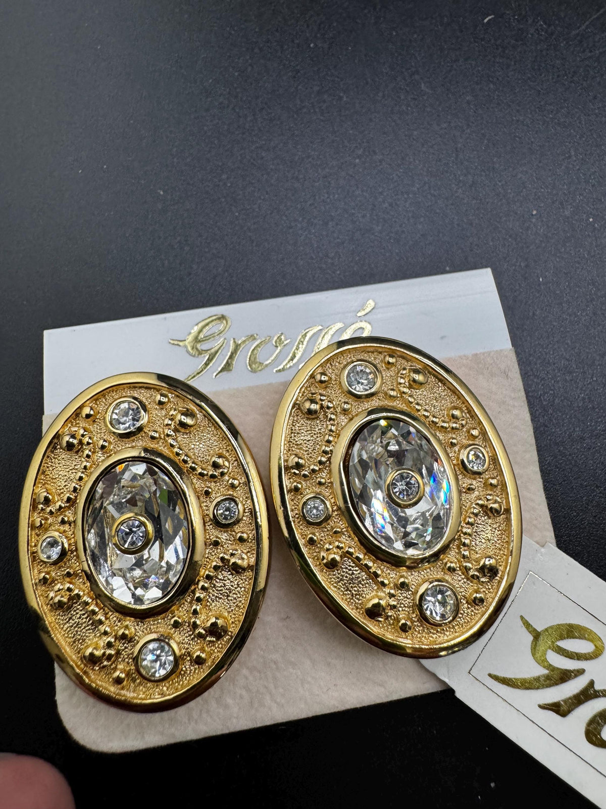 A pair of gold earrings with large, clear gemstones set in an oval-shaped design, displayed on a card with the word "Goré" written on it.