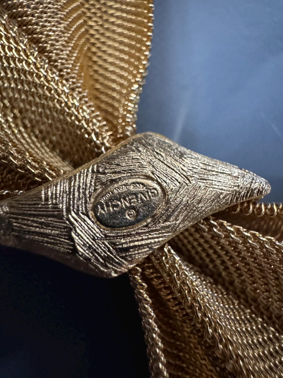 A close-up view of a gold-colored metal object, possibly a piece of jewelry or a decorative item, with a textured surface.
