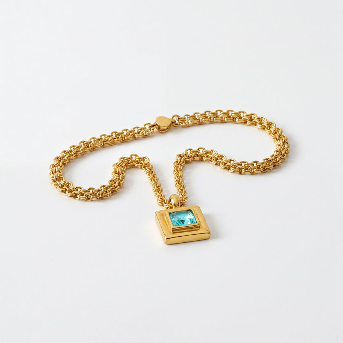 A gold chain necklace with a square pendant featuring a blue gemstone.