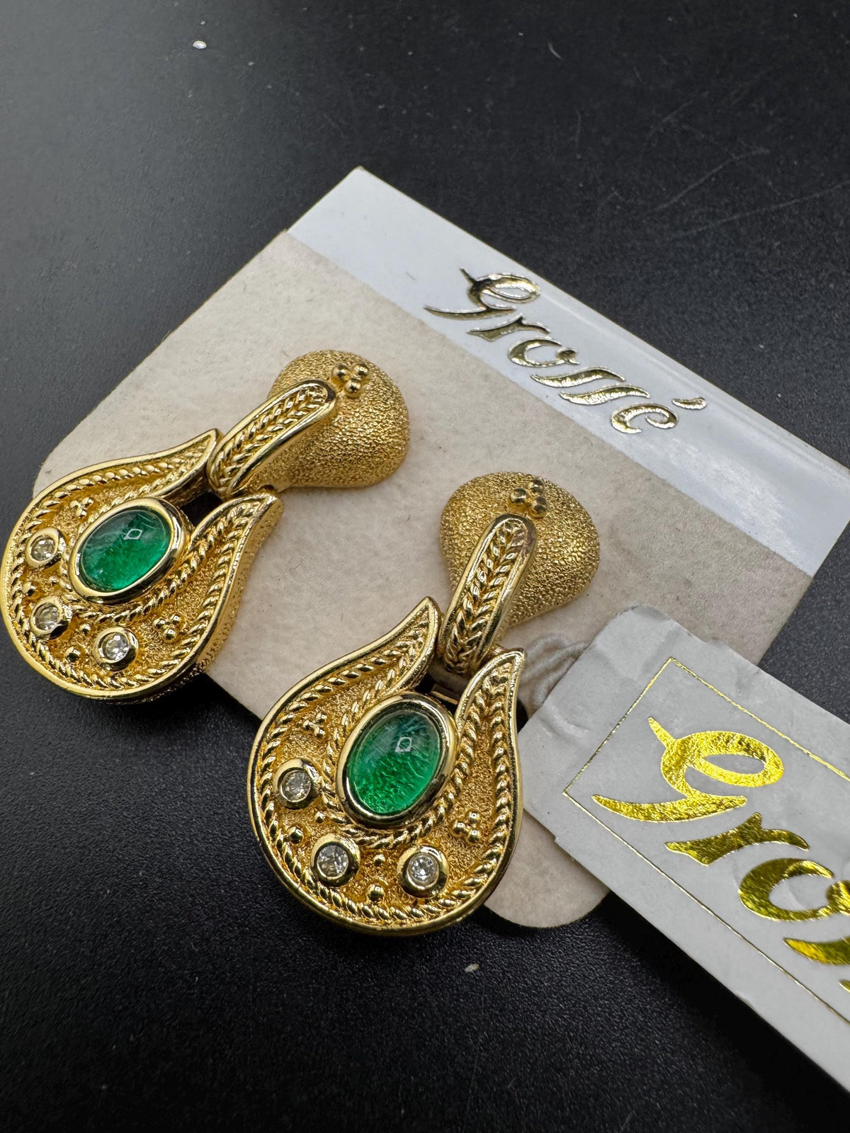 a pair of gold earrings with green gemstones, displayed on a black surface.