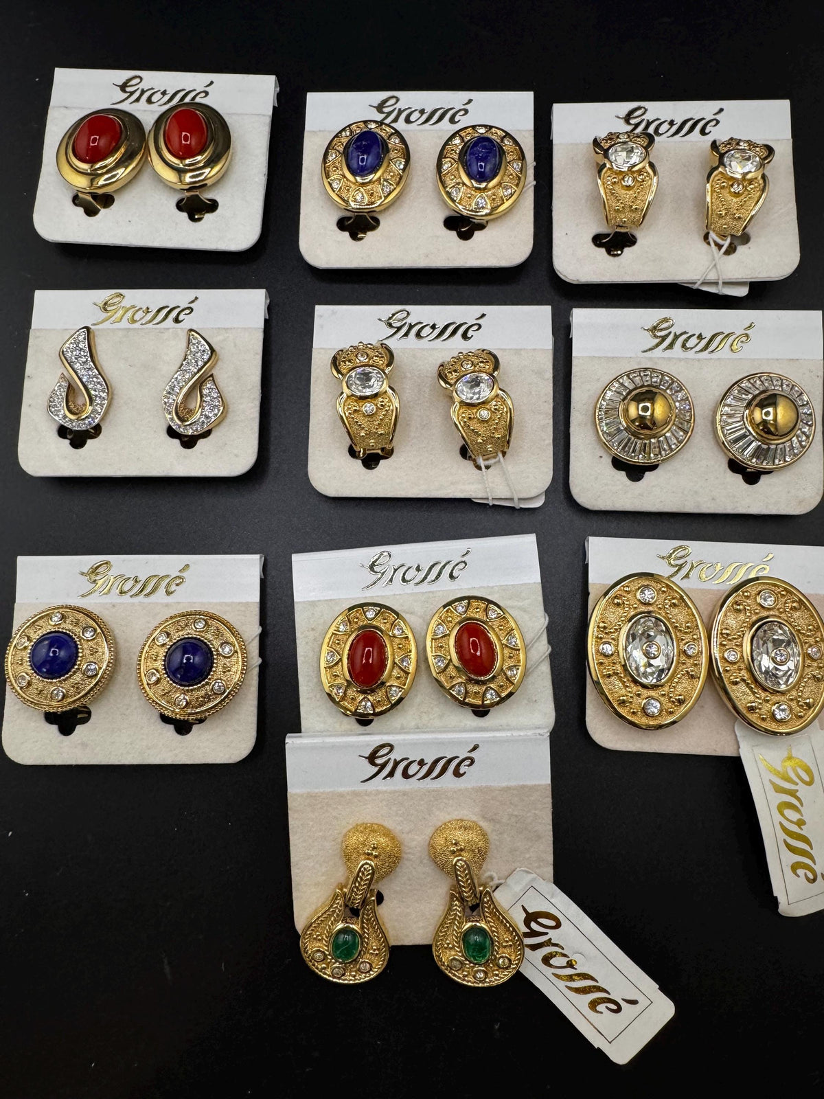 a collection of earrings with various designs and gemstones, presented on white cards with the brand name "Gros" printed on them.