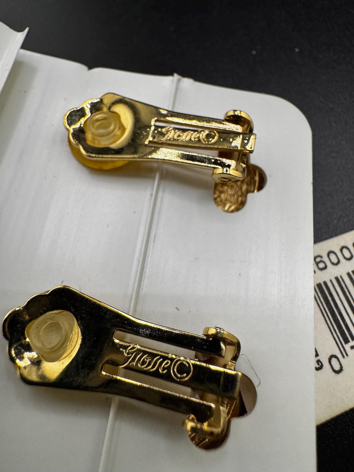 two gold-colored clip earrings with a floral design, resting on a white surface.