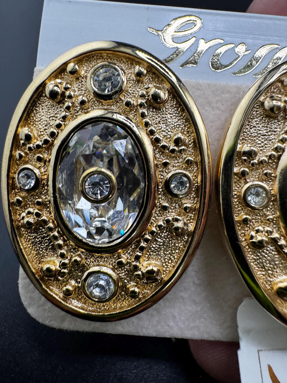 A close-up image of a pair of gold earrings with a large, clear gemstone in the center.