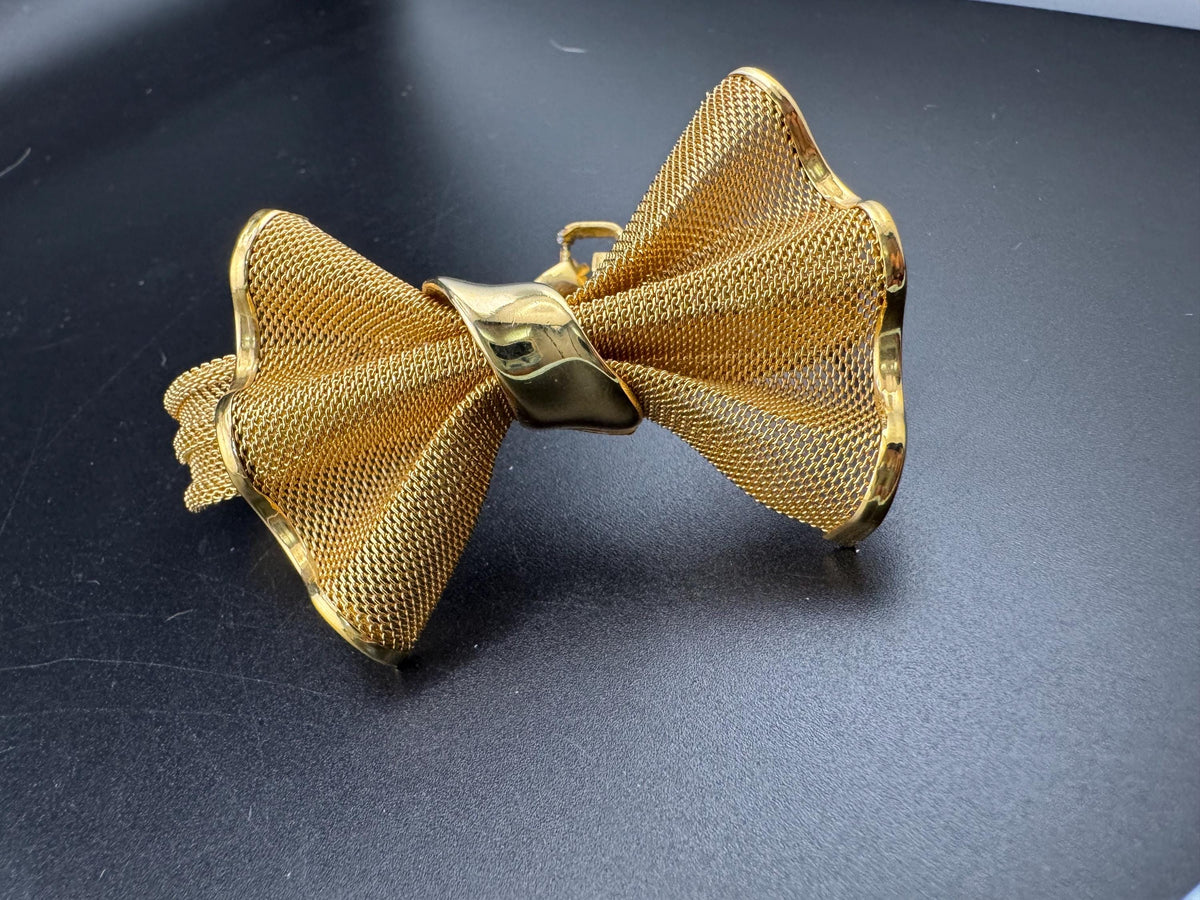 A gold-colored bow tie is shown against a dark background.