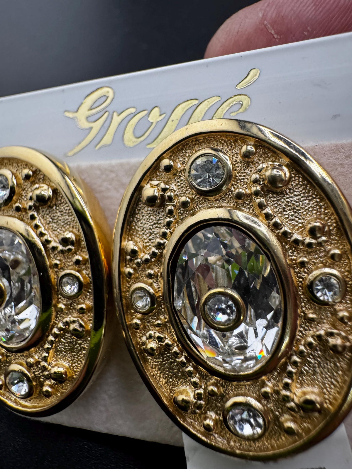 A close-up image of a pair of gold earrings with a large crystal center and a textured design around it.